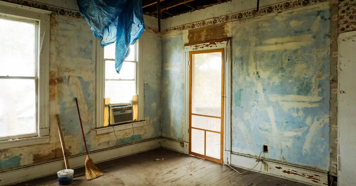 An empty room in an abandoned house with peeling walls and construction tools.